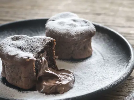 Deux coulants au chocolat inratables, saupoudrés de sucre glace, avec un cœur fondant qui déborde sur l'assiette.
