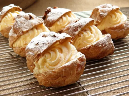 Pâte à choux au robot, garnies d'une crème onctueuse et saupoudrées de sucre glace, refroidissent sur une grille.
