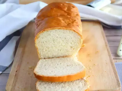 Un pain maison doré, tranché sur une planche en bois, parfait pour réussir son pain. La mie est aérée et la croûte appétissante.