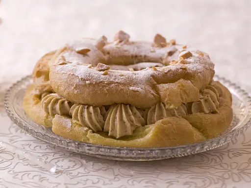Un Paris-Brest rond, saupoudré de sucre glace et d'amandes effilées, garni d'une généreuse crème diplomate.