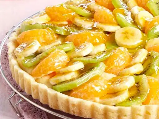 Tarte aux fruits frais sur une base de crème pâtissière. Des rondelles de banane, de kiwi et des quartiers d'orange sont disposés sur le fond de tarte.