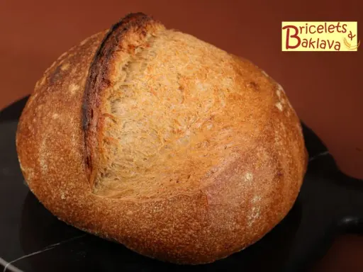 Belle miche de pain artisanal, prête après son temps de repos maximum. La croûte dorée et craquelée promet un délice.