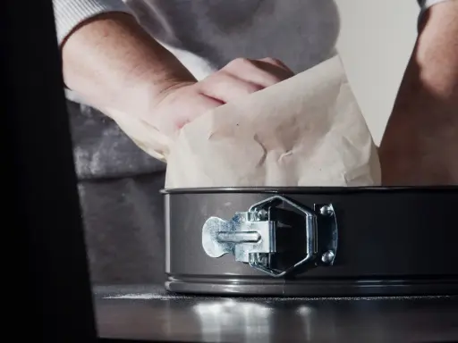 Mains expertes s'affairent à chemiser un moule avec du papier sulfurisé, préparant ainsi le terrain pour une future création culinaire.