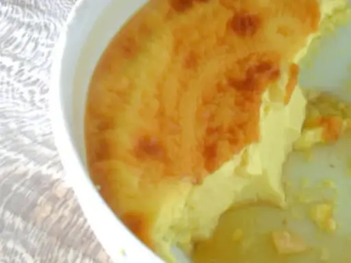 Un flan aux œufs à l'ancienne, doré et crémeux, servi dans un plat blanc sur une nappe texturée.