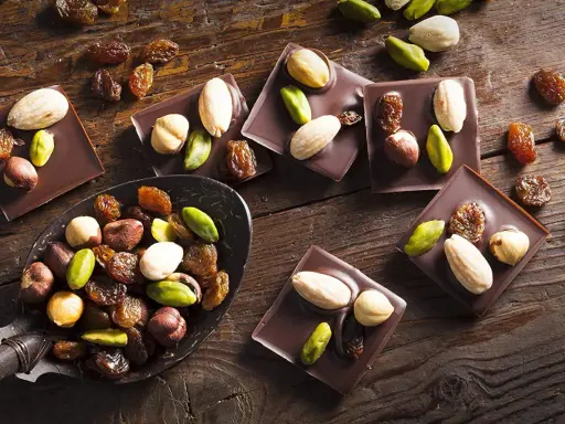 Carrés de chocolat noir Callebaut garnis d'amandes, noisettes, pistaches et raisins secs. Un délice à déguster !