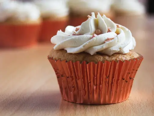 Un cupcake orné d'une généreuse ganache chocolat blanc, parsemé de perles rosées, dans un élégant caissette orange.