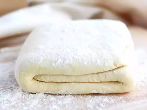 Pâte feuilletée prête à être utilisée pour votre recette. Les couches sont bien visibles, saupoudrées de farine.