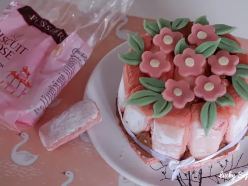 Charlotte aux biscuits roses de Reims, décorée de fleurs en pâte d'amande. Un biscuit rose saupoudré de sucre est à côté.