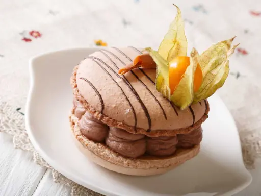Un délicieux macaron chocolat au lait, garni de crème onctueuse et décoré d'une physalis orangée.