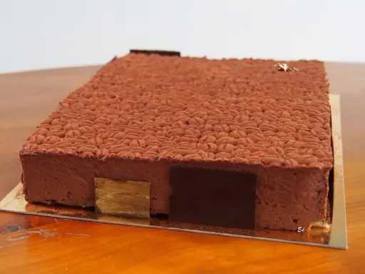 Gâteau rectangulaire au chocolat, décoré d'une texture rappelant des grains de café. Une recette insert crémeux café qui promet une dégustation exquise.
