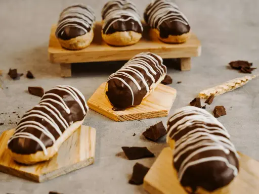 Éclairs gourmands avec un glaçage éclair chocolat brillant, décorés de fines rayures blanches. Des éclats de chocolat parsèment la table.