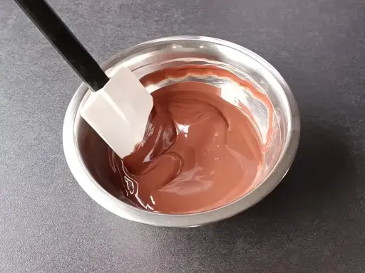 Spatule mélangeant une ganache au chocolat noir onctueuse dans un bol en métal.