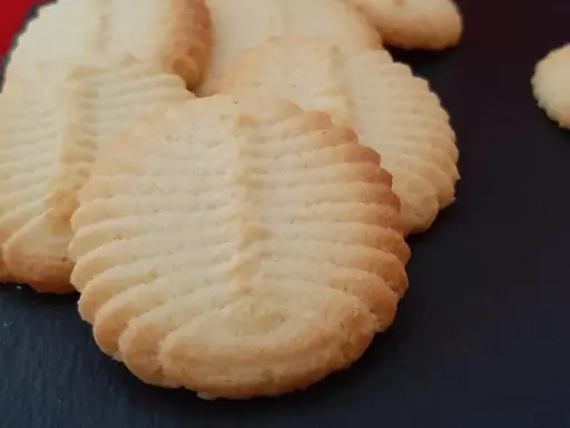 Un délicieux biscuit amande aux motifs striés, posé sur une surface sombre. Parfait pour accompagner un café.