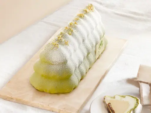 Bûche glacée verte, saupoudrée de sucre glace et de paillettes dorées, évoquant un biscuit madeleine.