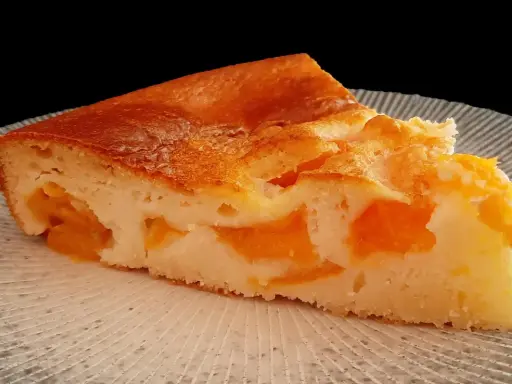 Tranche de clafoutis abricot, une création de chef, sur une assiette texturée.