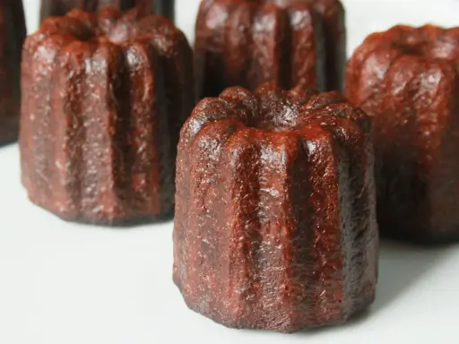 Plusieurs cannelés dorés, tout juste sortis du four, prêts pour la dégustation. La cuisson des cannelés révèle leur croûte caramélisée.