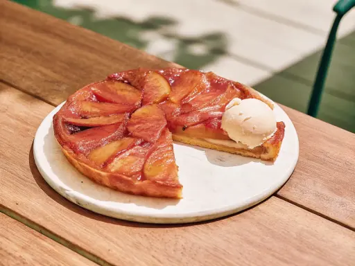 Tarte Tatin caramélisée, une part coupée, servie avec une boule de glace à la vanille. La cuisson parfaite révèle des pommes dorées et une pâte croustillante.