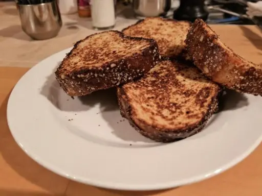 Quatre tranches de pain dur au four, dorées et croustillantes, sur une assiette blanche.