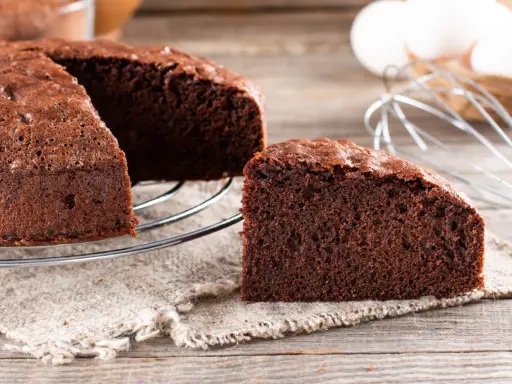Un délicieux gâteau génoise chocolat, moelleux et aéré, prêt à être dégusté. Des ingrédients frais comme des œufs et du cacao sont visibles en arrière-plan.