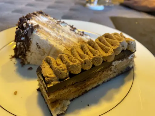 Deux parts de gâteau, dont une avec une crème légère et des copeaux de chocolat, l'autre un opéra conticini, sur une assiette blanche.