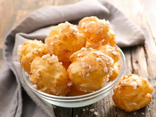 Un bol de chouquettes maison dorées et saupoudrées de sucre perlé, posé sur une table en bois.