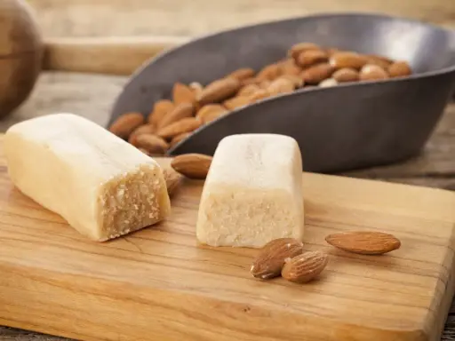Deux blocs de pâte d'amande et des amandes dans une pelle, prêts pour une recette de pâte d'amande maison.