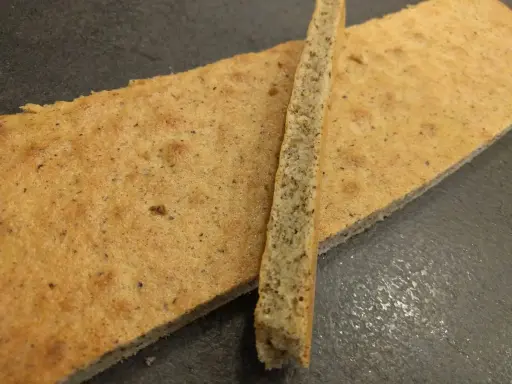 Deux fines tranches de biscuit joconde noisette, l'une posée sur l'autre, sur fond sombre.