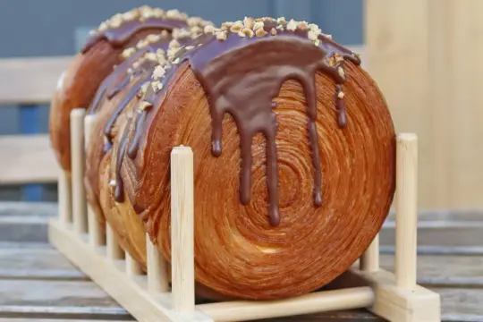 Un délicieux new york roll, feuilleté et garni de chocolat fondant et de noisettes concassées, présenté sur un support en bois.
