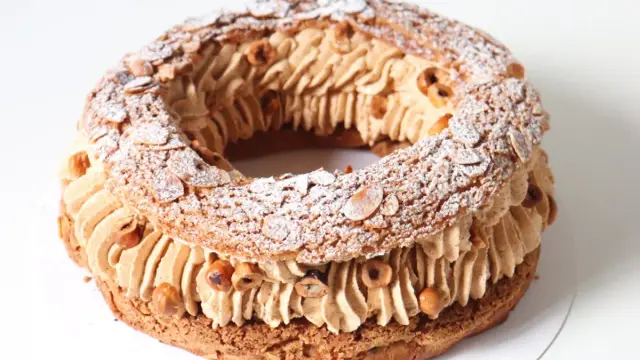 Un Paris-Brest rond garni d'une généreuse crème mousseline praliné, parsemé d'amandes effilées et de noisettes grillées.