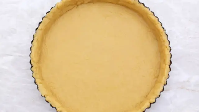 Une pâte brisée crue, prête pour la cuisson, est pressée dans un moule à tarte cannelé.