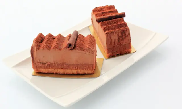 Deux parts de gâteau Trianon, le meilleur pâtissier, saupoudrées de cacao, sur une assiette blanche.