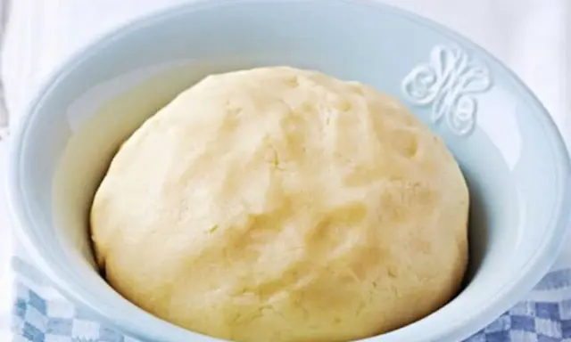 Pâte sablée prête pour la cuisson, dans un bol bleu clair. Une texture parfaite pour des tartes croustillantes.