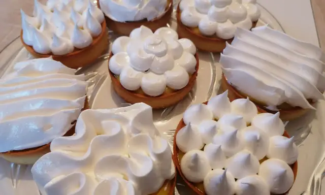 Assortiment de tartelettes garnies d'une crème citron et surmontées de **meringue italienne** aux formes variées.