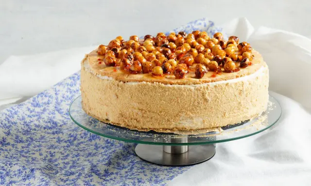Gâteau dacquoise noisette garni de noisettes caramélisées sur un présentoir en verre.
