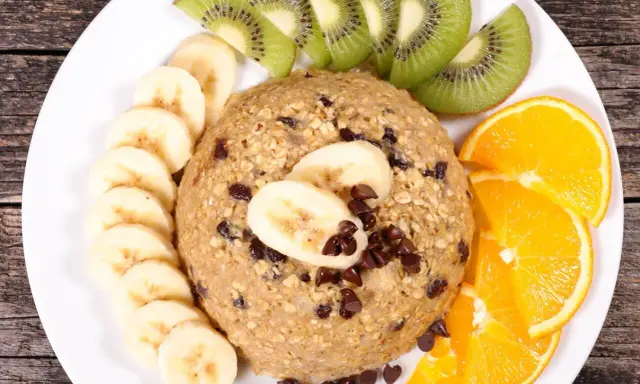 Un délicieux bowl cake flocon d'avoine garni de rondelles de banane, de tranches de kiwi et d'orange, parsemé de pépites de chocolat.