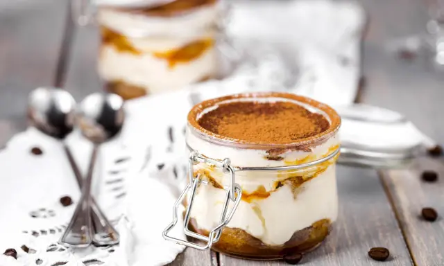 Deux bocaux de tiramisu, le meilleur dessert, saupoudrés de cacao, avec des grains de café et des cuillères sur une nappe en dentelle.