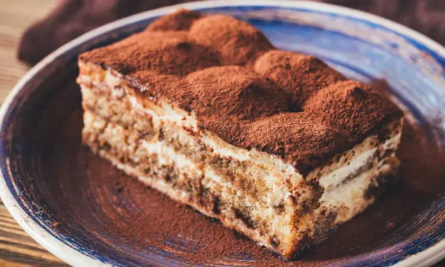 Tranche de tiramisu onctueux, saupoudrée de cacao, digne d'une recette tiramisu chef étoilé.
