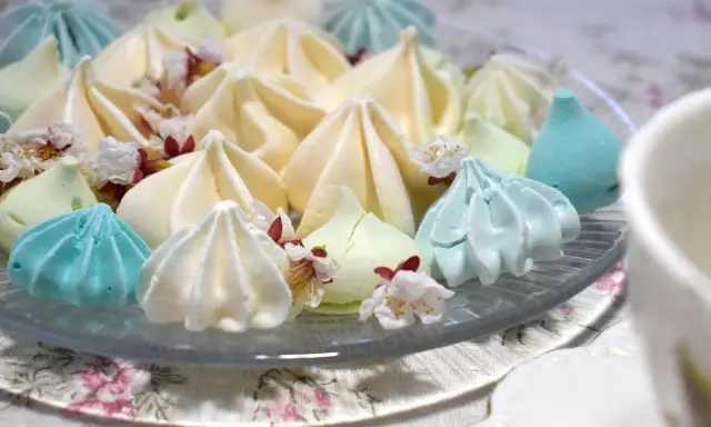 Meringues colorées, comme créées par un robot pâtissier, parsemées de fleurs délicates.
