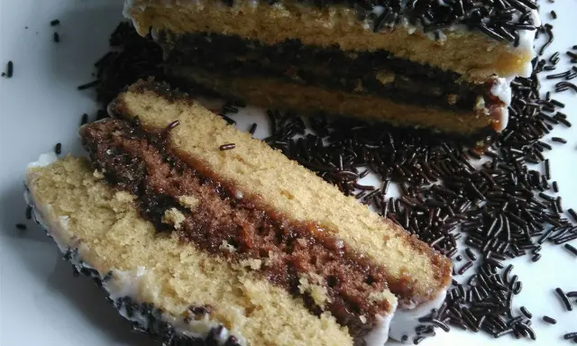 Délicieux napolitain maison, avec ses couches de génoise et de chocolat, nappé de glaçage blanc et saupoudré de vermicelles.