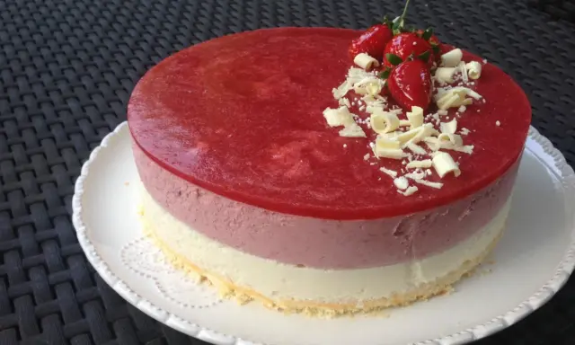 Un délicieux entremet aux trois couches, couronné d'une mousse fraise, de fraises fraîches et de copeaux de chocolat blanc. Parfait pour une occasion spéciale.