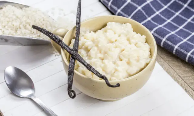 Un bol de riz au lait crémeux, garni de gousses de vanille, avec du riz brut à côté.