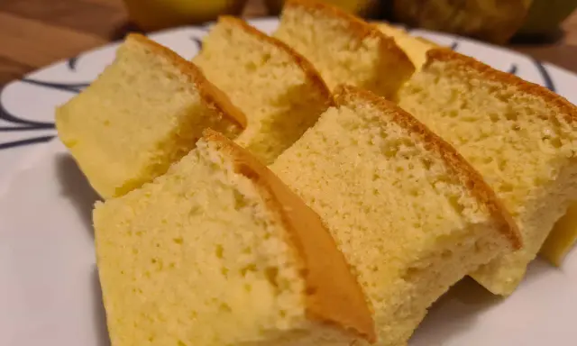 Tranches de moelleux gâteau japonais, léger et aérien, sur une assiette blanche. Des fruits jaunes sont flous en arrière-plan.