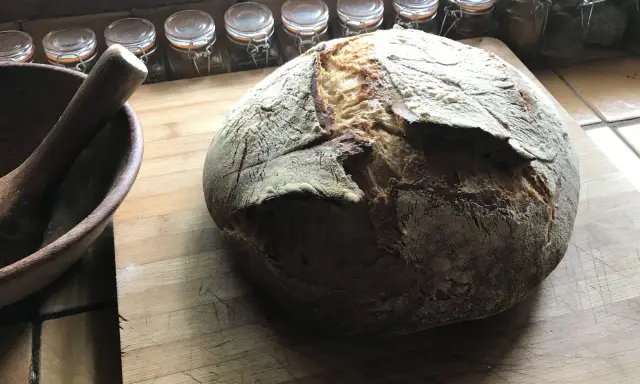 Gros pain artisanal sur une planche en bois, avec un mortier à côté. La question "peut on mélanger levain et levure" plane dans l'air.