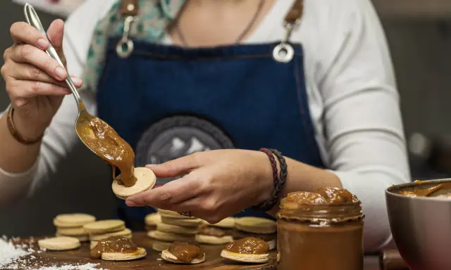 Une main dépose une cuillère de dulce de leche sur un biscuit rond, préparant des **caras crakine fait maison**.