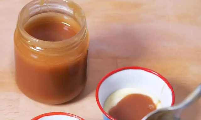 Un pot de caramel beurre salé sans beurre demi sel, prêt à être dégusté. Une cuillère est sur le point de plonger dans une petite coupelle de crème et de caramel.