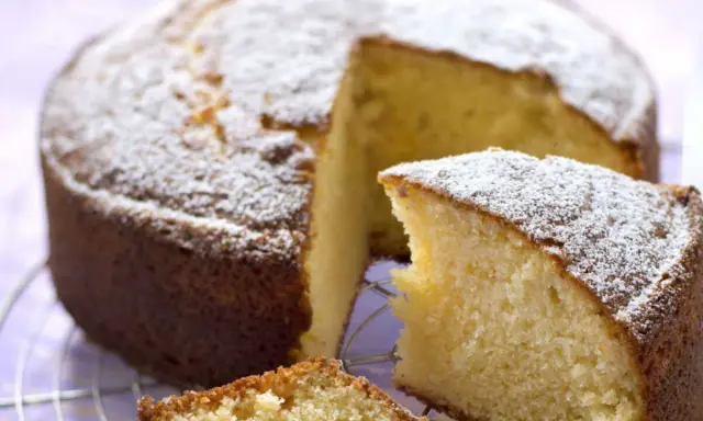Un délicieux gâteau sans oeuf, saupoudré de sucre glace, attend sur une grille. Une part est déjà coupée, révélant sa mie moelleuse.