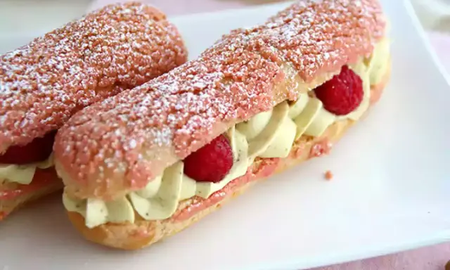 Deux éclairs à la framboise, garnis de crème légère et de fruits rouges, saupoudrés de sucre glace.