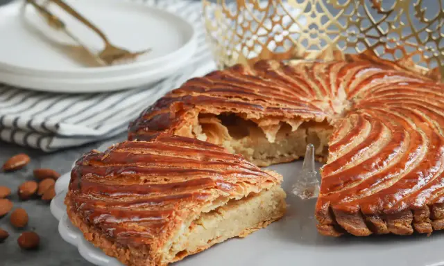 Galette des Rois dorée, garnie d'une généreuse crème d'amande. Une part est coupée, révélant sa texture feuilletée.