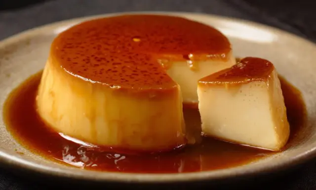 Crème renversée on a plate, with a slice cut out, glistening with caramel sauce.