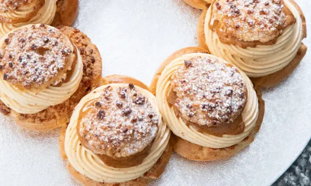 Plusieurs Paris-Brest, des pâtisseries rondes à la pâte à choux garnies de crème onctueuse et saupoudrées de sucre glace et d'amandes.